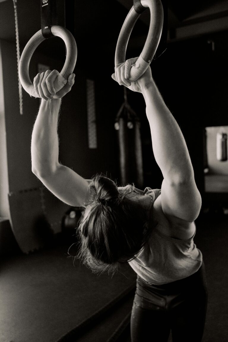 Man performing strength training with gymnastic rings in gym setting.